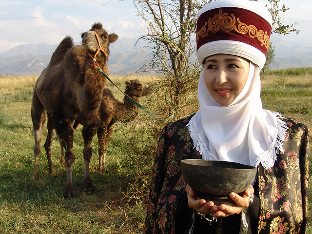 Kyrgyz woman wearing a traditional outfit with a bactrian camel and its calf, Kyrgyzstan